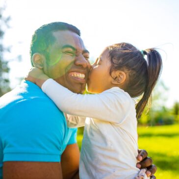 Little girl giving her dad a kiss on the cheek while he smiles