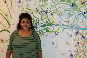 woman in green striped shirt smiling in front of tree of life mural